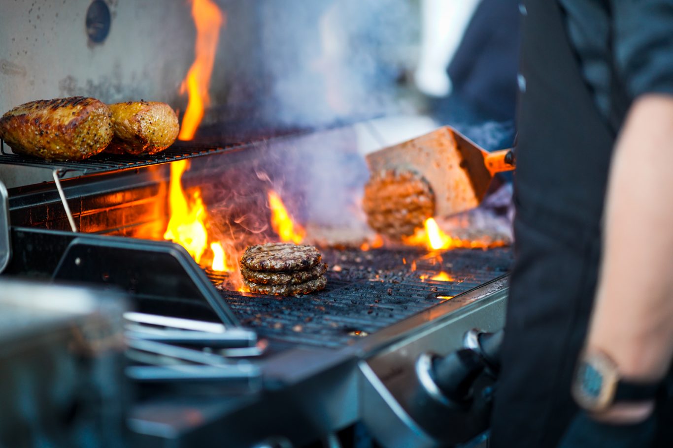 Fleischburger grillen über offenen Flammen, mit Funken und glühender Kohle.