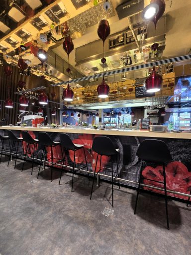 Moderne Bar mit Holztheke, schwarzen Stühlen und roten Lampen in einem stilvollen Restaurant.
