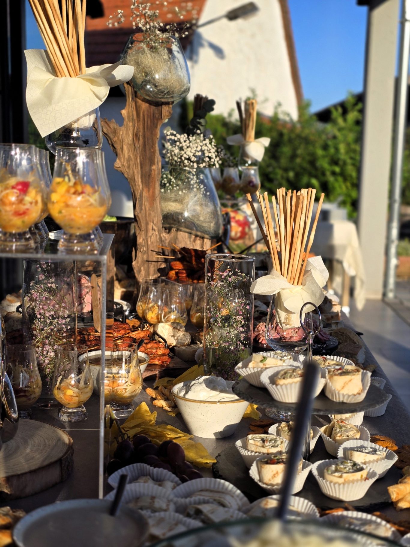 Festlich gedecktes Buffet mit Snacks, Früchten, Dips und dekorativen Elementen im Freien.