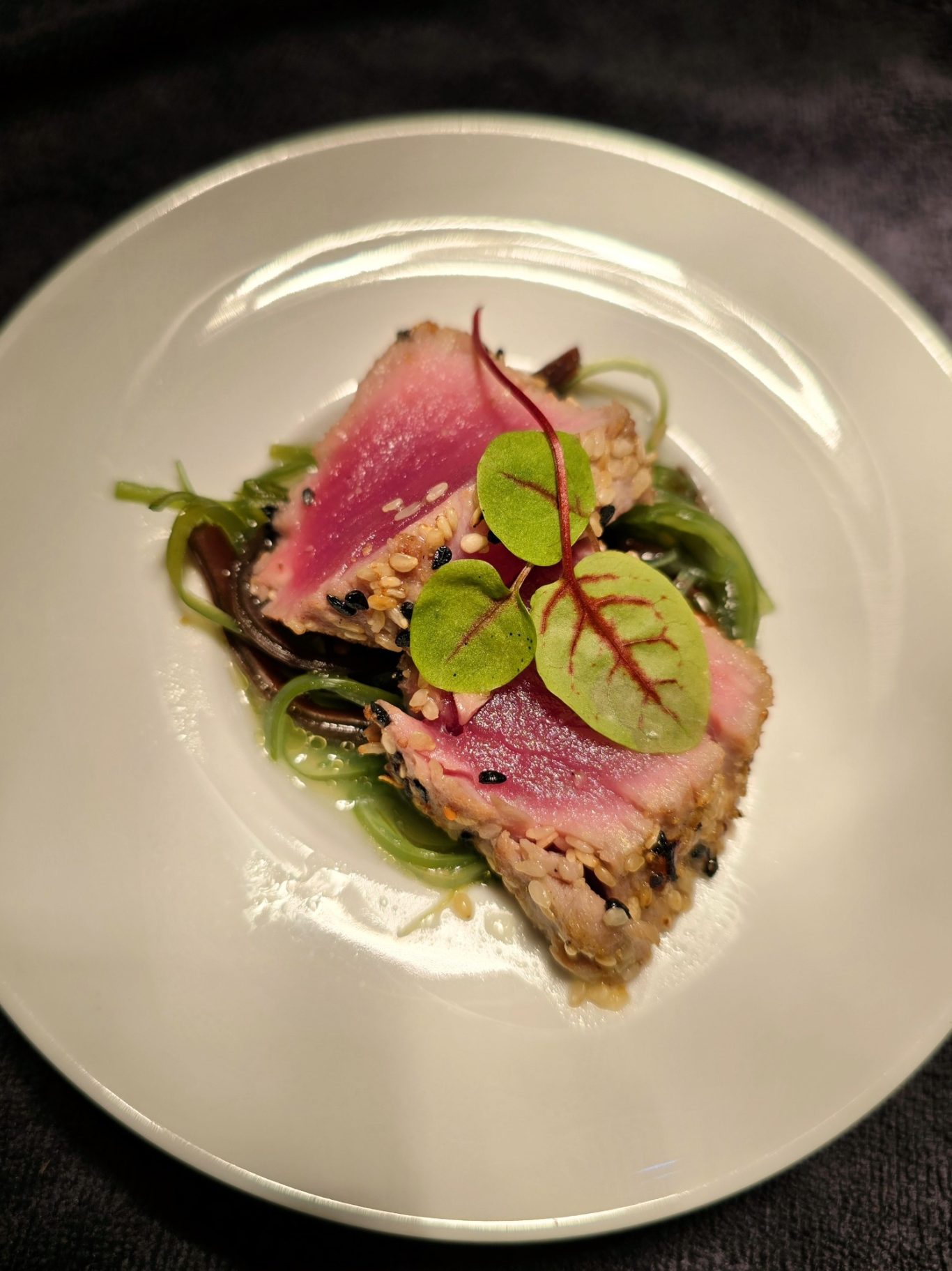 Rohes Thunfischsteak auf einem Bett aus Algen mit frischen Kräutern.