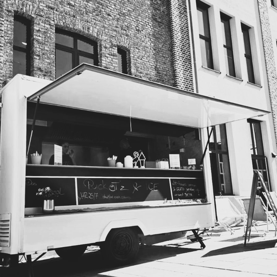 Ein Foodtruck mit öffentlichem Verkaufsfenster vor einer Backsteinmauer.