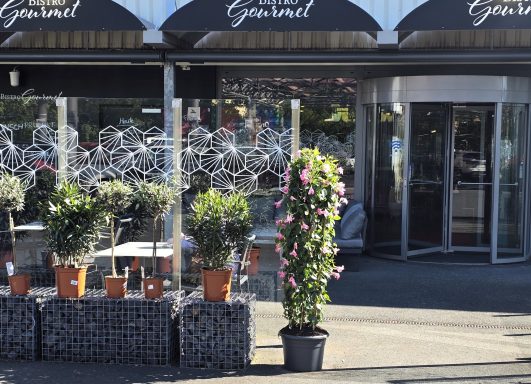 Blumen und Pflanzen in Töpfen vor einem Restaurant mit Glasschiebetüren.